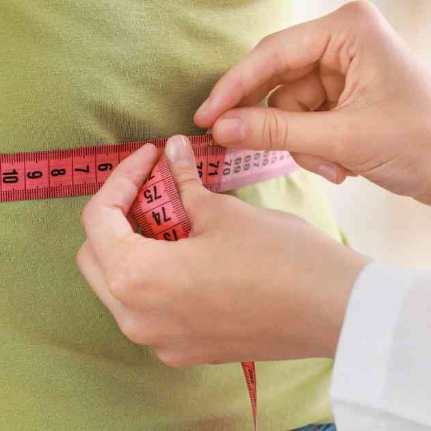 girl in green shirt having her waist measured by doctor